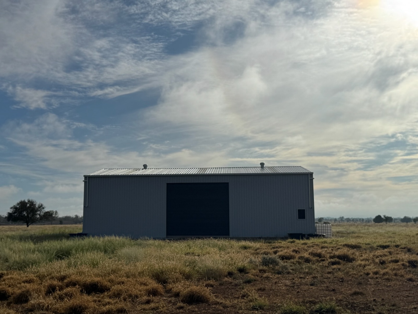 A large corrugated iron machinery shed situated on the grassy paddock under a vast sky