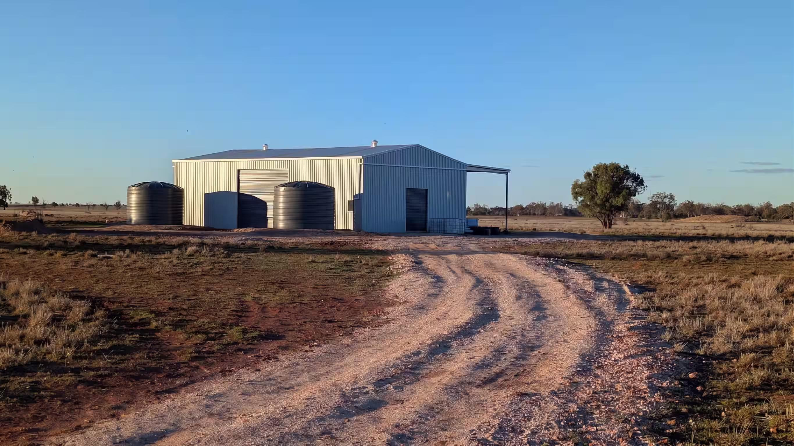 Wide angle approach to corrugated machinery shed across paddock